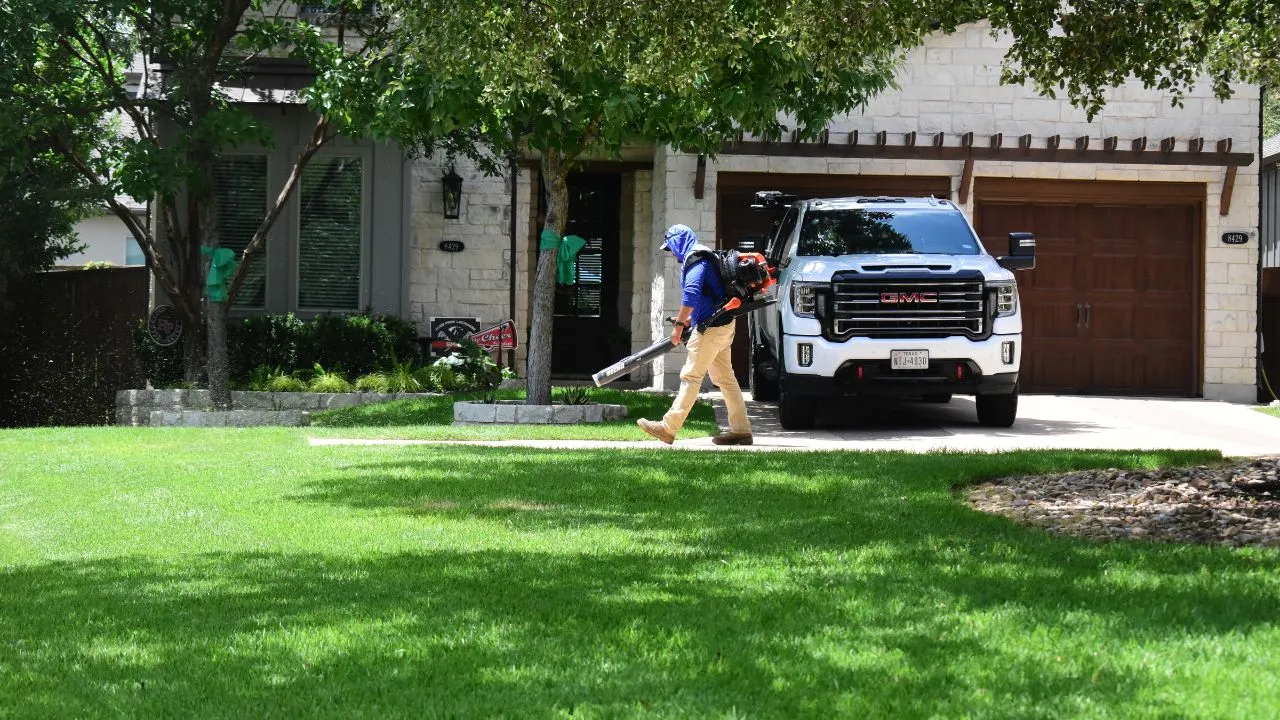 Man with a backpack blower blowing blades of grass of sidewalk in front of home